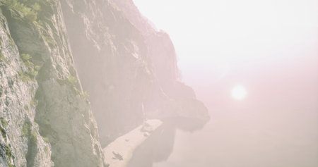 Breathtaking cliffs rise over calm waters reflecting the warmth of the sunset. A tranquil beach lies below, creating a peaceful atmosphere during twilight hours.の写真素材