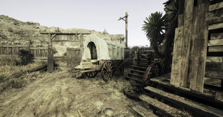 A weathered wooden wagon rests near an old structure in a deserted town. Dusty paths and sparse vegetation create a desolate atmosphere under a clear sky.の写真素材