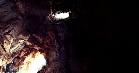 In a deep cave, beams of light penetrate the darkness, illuminating rugged rock formations. The...