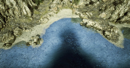 Crystal clear blue water meets a sandy beach, framed by rugged cliffs. Sunlight glimmers on the surface, creating a serene and peaceful atmosphere.の写真素材