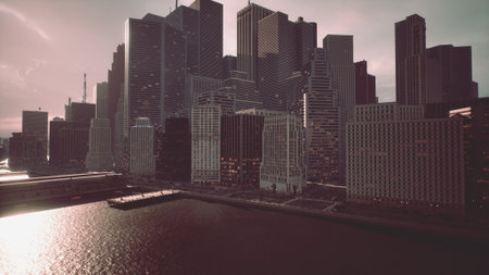 Skyscrapers tower over a shimmering river during sunset, casting long shadows. The scene captures the beauty of urban architecture and vibrant city life, inviting awe in its grandeur.の写真素材