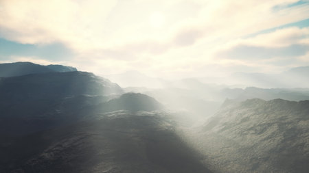 Dramatic view of a mountain range shrouded in mist, sunlight streams through clouds, creating a serene and mystical atmosphere in a remote location during early morning hours.の写真素材