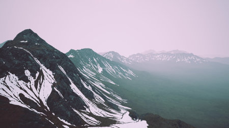 Snow capped peaks rise dramatically in the early morning light, shrouded in mist. The rugged terrain showcases stunning slopes and valleys, creating a breathtaking landscape.の写真素材
