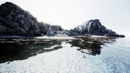 A serene coastal scene shows clear water mirroring rugged rocks and a distant shoreline. Soft light...