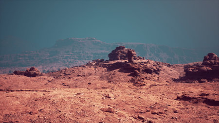 Vast red rock formations rise against a blue sky, creating a surreal landscape. The terrain appears dry and rugged, with distant mountains adding depth to the scene.の写真素材