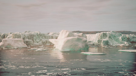 Icebergs float gracefully on the serene waters of the Arctic. The landscape features majestic, shimmering ice formations under a pale sky during the tranquil afternoon.の写真素材