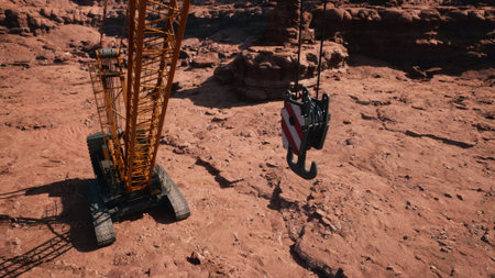 A large crane stands on rugged red earth, its hook suspended in the air. The scene captures the intensity of construction work in a remote, sunlit landscape, highlighting the intricate task at hand.の写真素材