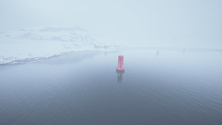 A bright red buoy floats in serene, misty waters surrounded by snow covered land, creating a peaceful winter scene filled with fog and tranquility.の写真素材