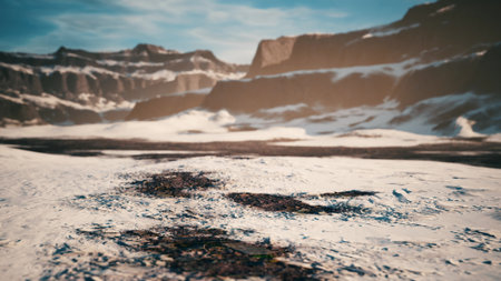 A breathtaking view of a snowy terrain surrounded by towering rocky mountains. The bright sunlight casts a warm glow, revealing the beauty of natures winter wonderland.の写真素材