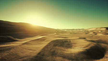 A serene early morning in the desert reveals gentle rolling dunes bathed in golden sunlight. The horizon stretches infinitely under a clear blue sky, creating a peaceful atmosphere.の写真素材