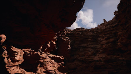 Bright sunlight casts shadows on the striking red rock formations, creating a contrast with the soft, fluffy clouds above. A majestic scene of nature unfolds, inviting exploration.の写真素材