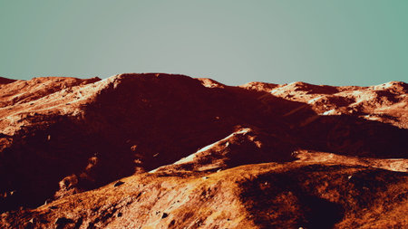 Shadows stretch across rugged mountain ridges as the sun sets. The landscape is bathed in warm hues, creating a perfect scene for nature lovers and adventurers alike.の写真素材