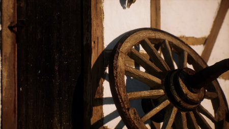 A vintage wooden wheel leans against a weathered door of a traditional building. Sunlight casts soft shadows, highlighting the textures of wood and the charming countryside atmosphere.の写真素材
