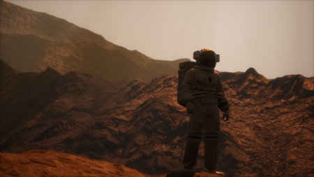 An astronaut stands on the rocky surface of a foreign world, gazing at majestic mountains under a soft, glowing sky during a serene moment of exploration and discovery.の写真素材