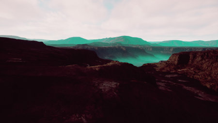 High above a dramatic and vast mountain range, rolling hills and jagged cliffs create a stunning panorama. The clouds drift softly, casting an ethereal glow over the scenery.の写真素材