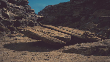 A large, flat rock sits precariously between towering cliffs, casting a shadow on the sandy ground....