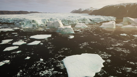 Bright icebergs drift serenely in dark waters, illuminated by gentle sunlight. The surrounding mountains create a stunning backdrop, showcasing natures beauty in this remote location.の写真素材