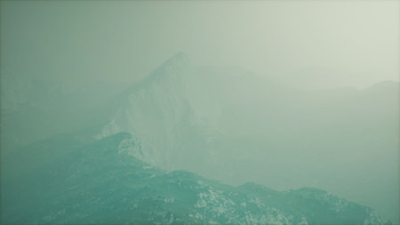 A serene mountain landscape engulfed in mist, creating a mysterious atmosphere. Soft light filters through the fog, highlighting the rugged terrain.の写真素材