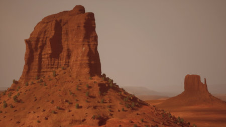 Towering red rock formations dominate the expansive desert landscape of Utah. The sun casts warm hues across the rugged terrain as shadows dance on the hills, creating a breathtaking view.の写真素材