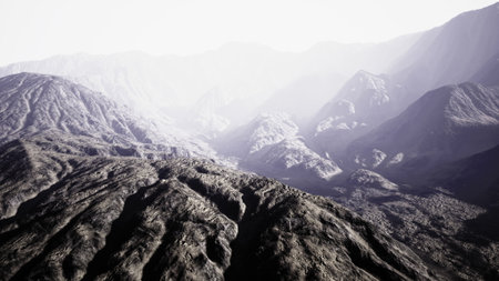 Early morning reveals a breathtaking scene where mist gently caresses the rugged mountain range. The soft light adds drama to the rocky terrain, creating a serene yet powerful atmosphere.の写真素材