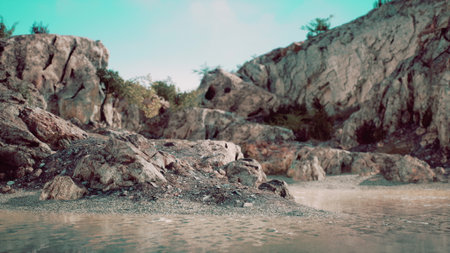 A picturesque landscape features rugged rocks beside tranquil water. The greenery surrounds the rocky formations, creating a peaceful environment under a clear sky.の写真素材