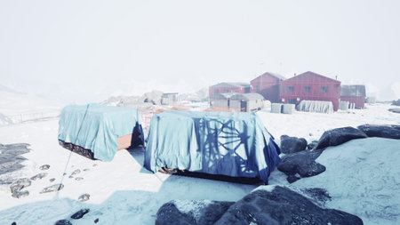 Snow blankets the rugged terrain as colorful buildings peek through the frost. Research equipment is shielded by tarps, hinting at scientific exploration amidst a serene winter wonderland.の写真素材