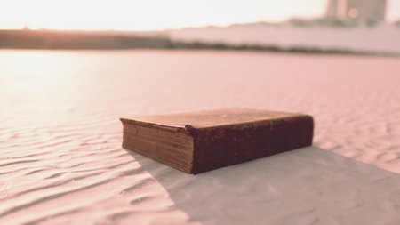 A weathered book lies open on soft, golden sand dunes, bathed in the warm glow of a vibrant sunset. The fading light enhances the allure of the setting, sparking curiosity.の写真素材