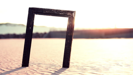 In a serene desert landscape, a striking black frame stands upright in the soft sand. The warm sunlight casts a golden hue, creating a captivating atmosphere that invites creativity and reflection.の写真素材