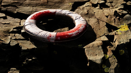 A weathered lifesaver ring lies on textured rocks by the waters edge, catching the warm glow of the golden hour. The scene portrays tranquility and the beauty of natures elements.の写真素材