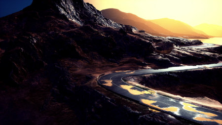 A winding road curves through majestic mountains as the sun sets, casting a warm glow on the...