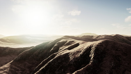 Rolling hills stretch across the landscape, bathed in warm sunlight as the sky gently brightens. This peaceful scene captures the beauty and tranquility of nature in a vast open space.の写真素材