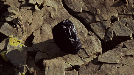 A black bag sits alone on uneven rocky terrain, illuminated by the soft glow of the afternoon sun. Shadows stretch across the surface, creating an intriguing contrast.の写真素材