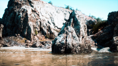 A large rock stands majestically in calm waters under a bright blue sky. Breathtaking scenery showcases rugged terrain and lush greenery in the background, highlighting natures beauty and serenity.の写真素材