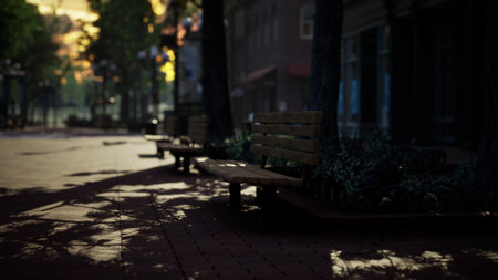 Desolate park benches line a quiet street as the sun sets, casting long shadows and bathing the surroundings in warm, golden light. Nature and stillness unite in this tranquil moment.の写真素材