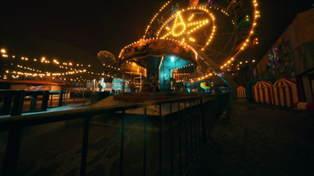The amusement park remains silent at night, featuring brightly lit rides and stalls, showcasing a vibrant but unoccupied atmosphere as colorful lights illuminate the dark surroundings.の写真素材