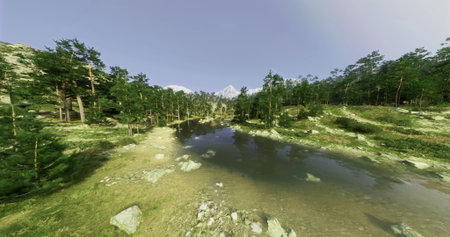 A peaceful forest landscape features a calm river surrounded by lush greenery and towering trees. Majestic mountains rise in the background under a clear sky.の写真素材