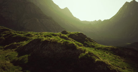 Sunlight gently illuminates a vibrant green hillside surrounded by majestic mountains. The tranquil scene captures natures beauty at dawn, evoking a sense of peace and wonder.の写真素材