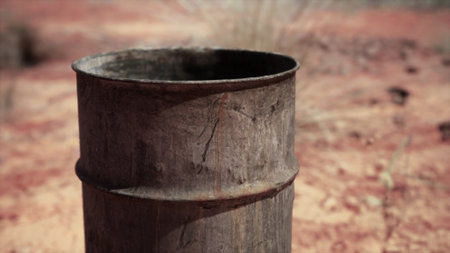 A weathered metal drum stands solitary on the dry, cracked ground. Sunlight highlights its rustic charm in a stark landscape, evoking a sense of isolation and endurance of nature.の写真素材