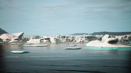 In a tranquil landscape, massive icebergs drift slowly across a serene body of water. The sunlight reflects off the icy surfaces, creating a magical atmosphere. Mountains rise in the background.の写真素材