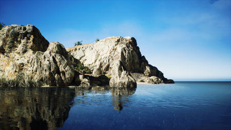 The stunning rocky coastline stands tall against a clear blue sky, its reflection shimmering in the tranquil waters. A serene moment captures natures beauty and tranquility.の写真素材