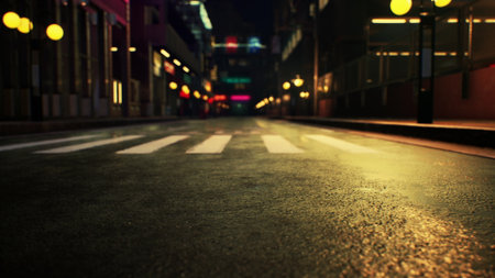 A quiet urban street at night shows wet pavement reflecting colorful lights from nearby buildings. Empty crosswalks hint at a moment of calm in a lively city atmosphere.の写真素材