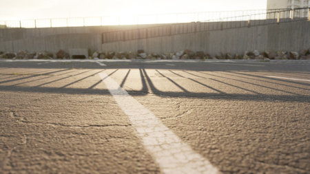 Golden sunlight bathes an empty parking lot, creating delicate shadows from a nearby fence. The peaceful scene captures the serene beauty of dusk.の写真素材