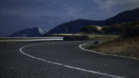 A winding road curves gracefully through a serene mountainous landscape as twilight descends. Shadows lengthen and the sky deepens, creating a calm and tranquil atmosphere.の写真素材