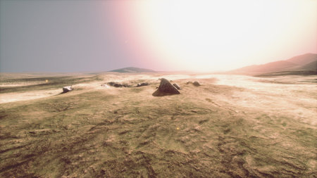 A vast, barren landscape stretches under a glowing sunset. Rocky formations dot the sandy ground, while soft light creates shadows on the surface.の写真素材