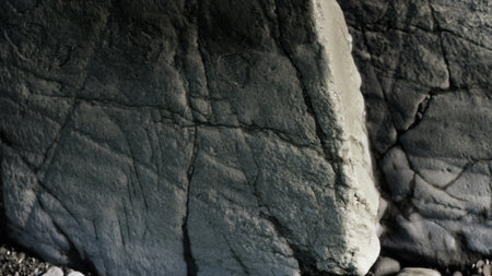 A rugged rock surface displays intricate textures and patterns shaped by time. The soft light...