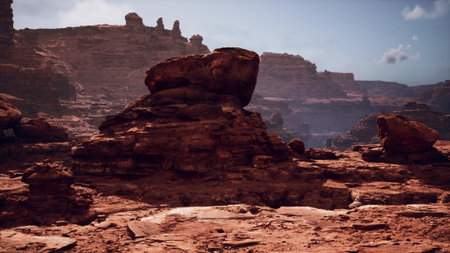 In a sprawling desert scene, majestic rock formations rise against a clear blue sky. Sunlight casts shadows on rugged terrain, highlighting various textures of stone and earth.の写真素材