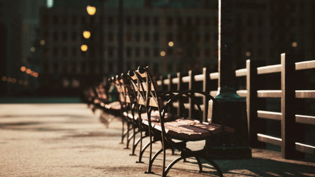 Sunlight casts a warm glow on empty wooden benches along a riverside promenade. A gentle breeze rustles leaves as the day transitions to evening, creating a serene atmosphere.の写真素材