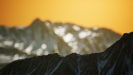 Dramatic peaks rise against a brilliant orange sky as the sun sets over the horizon, casting a warm glow on the snow capped mountains. The landscape reflects serene beauty and tranquility.の写真素材