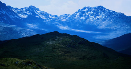 Breathtaking mountains rise dramatically against the horizon, adorned with snow caps and deep blue tones, surrounded by verdant valleys and rugged terrain under a serene sky.の写真素材