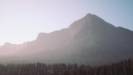 In this serene scene, the sun rises over a majestic mountain, casting a gentle glow over the rugged peak. Tall trees surround the base, creating a peaceful atmosphere in natures embrace.の写真素材
